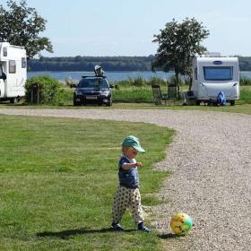 Lille dreng leger med en bold på plæne på Horsens City Camping med campingvogne og Horsens Fjord i baggrunden